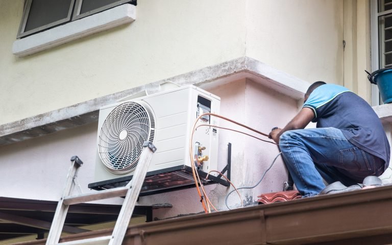 Technician installing outdoor air conditioner compressor unit on outdoor wall